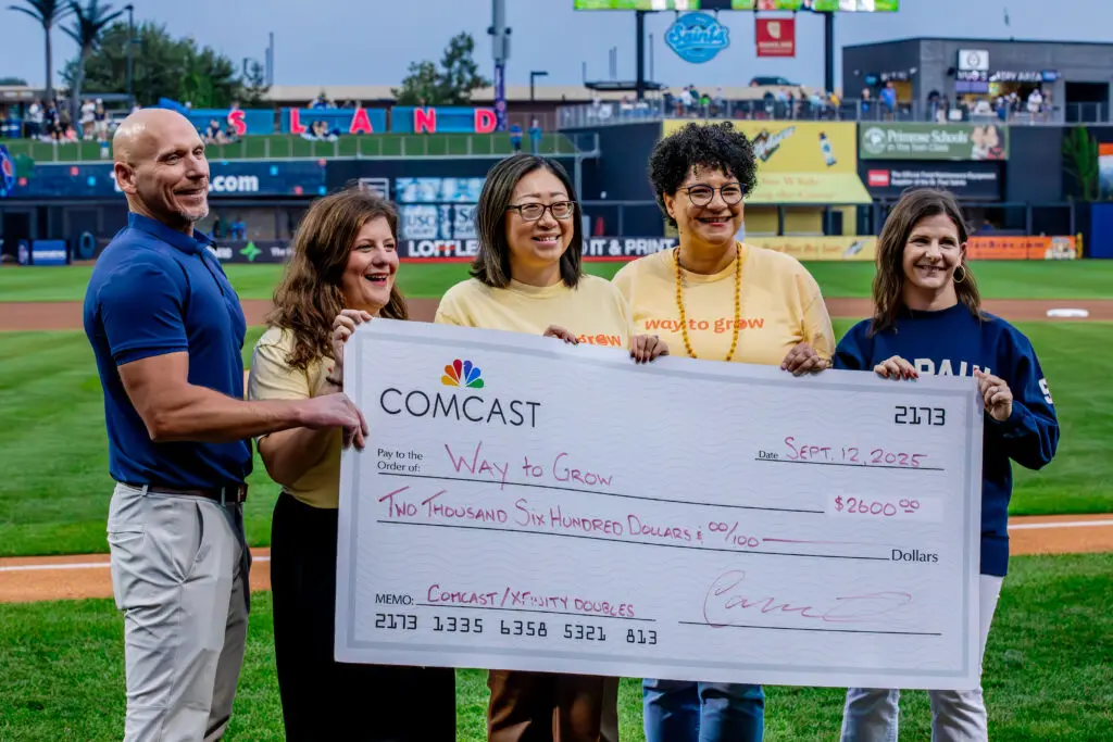 Five people standing on a baseball field holding a check