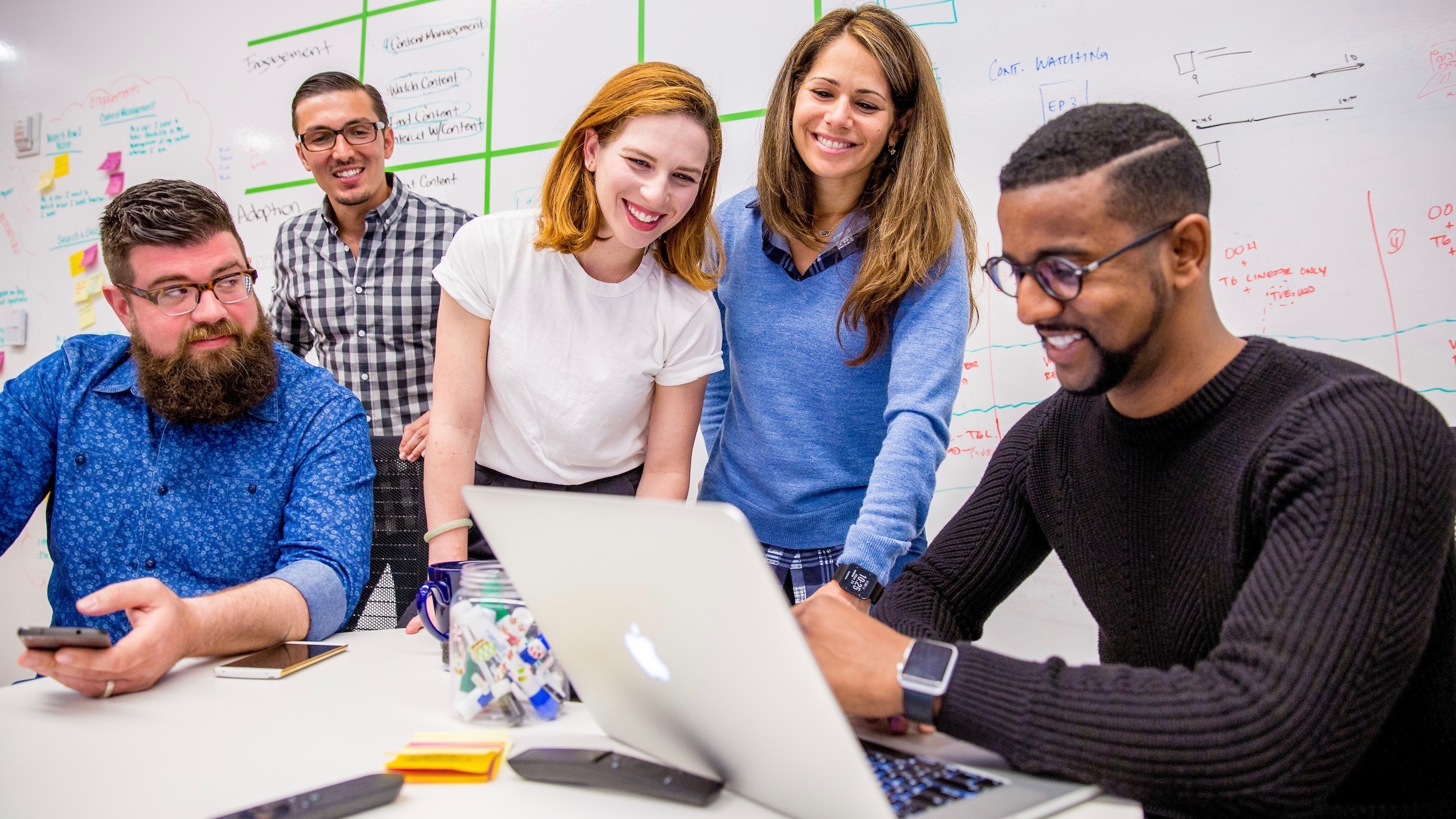 Five coworkers gather around a laptop.