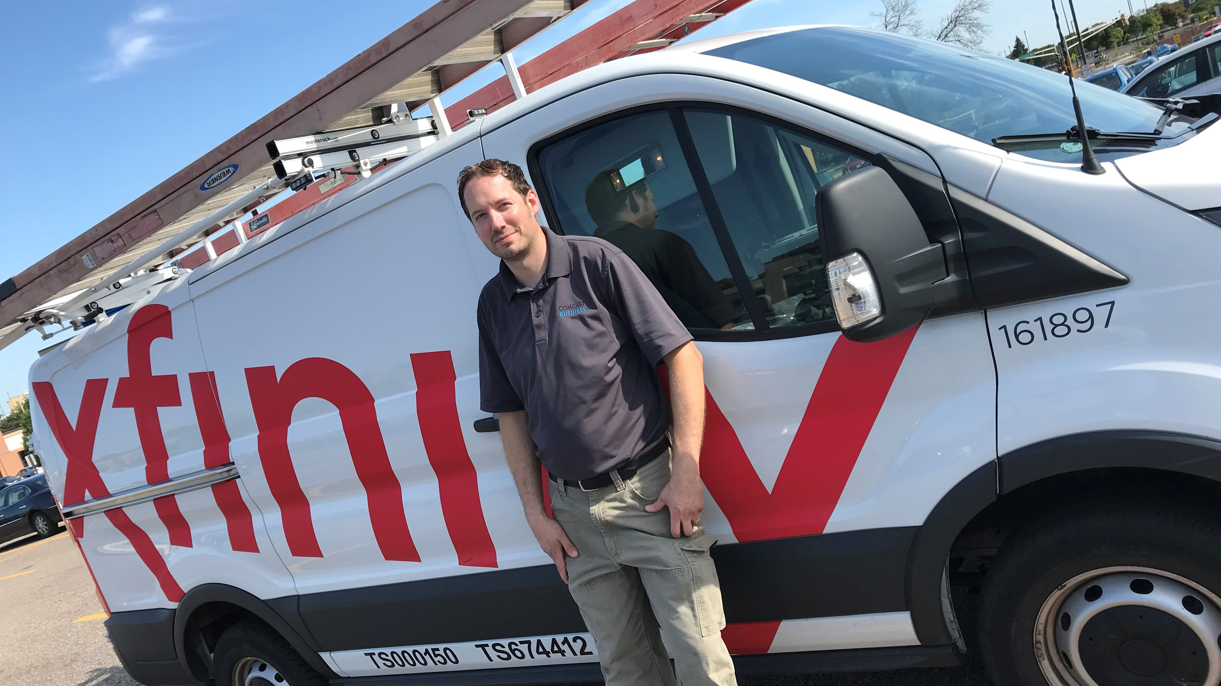 An Xfinity technician stands next to an Xfinity van.